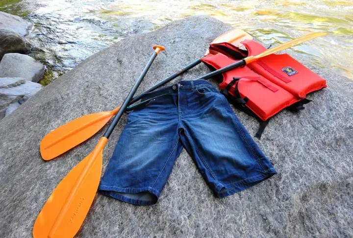 Wet cotton shorts unsuitable for whitewater rafting discarded next to appropriate synthetic gear by a river.