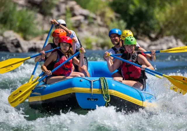 Diverse group of rafters wearing helmets paddling fearlessly through whitewater rapids.