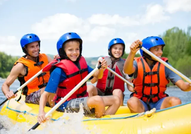 Happy family with kids wearing safety gear, enjoying a sunny rafting trip on a moderate river, illustrating kid-approved vacation planning.