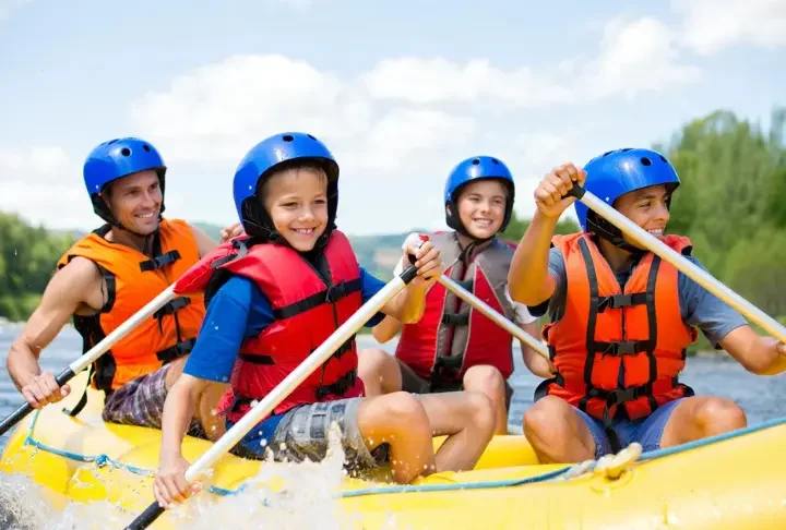 Happy family with kids wearing safety gear, enjoying a sunny rafting trip on a moderate river, illustrating kid-approved vacation planning.