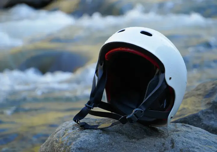 Whitewater helmet on a rock near rapids, highlighting why helmets matter for rafting safety against river hazards.