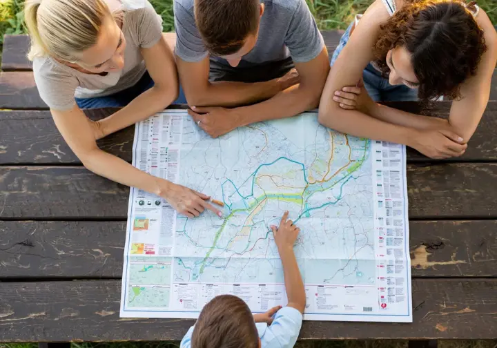 Family looking at a river map together in bright daylight, representing the selection of appropriate river adventures.