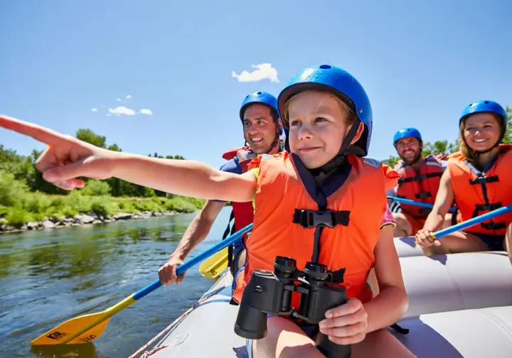 Young girl excitedly using binoculars on a raft during a sunny family trip, showing kid engagement and fun.