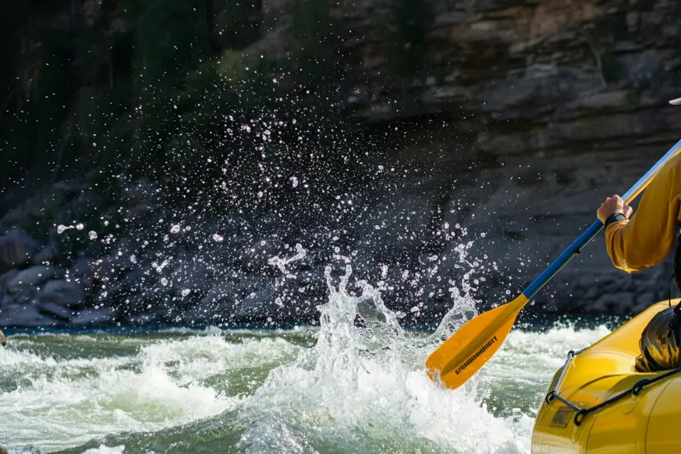 A close-up of a rafter navigating the rapids on the Colorado River with splashing water and rugged scenery.  