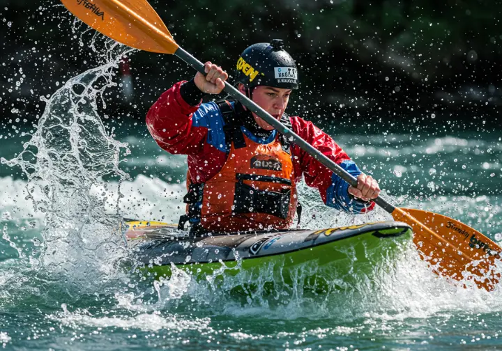 Rafter paddling with water splashing, showcasing appropriate gear for a rafting adventure.