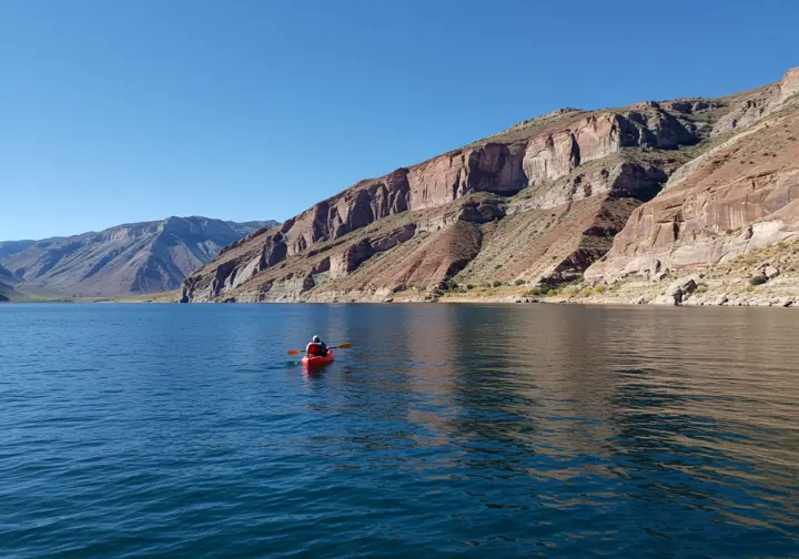 Flaming Gorge kayaking adventures: kayak on calm blue water surrounded by dramatic red cliffs.