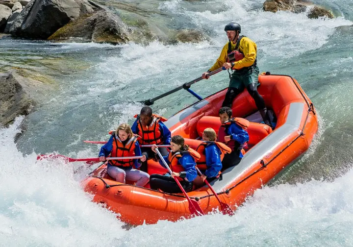 Professional guide steering a commercial raft with passengers through sunlit rapids on the Middle Fork Salmon River, representing outfitter services.