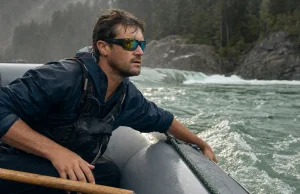 Best Polarized Sunglasses for Rafting That Float Rafter in a raft reading the river line wearing polarized Smith Optics sunglasses on a gray morning