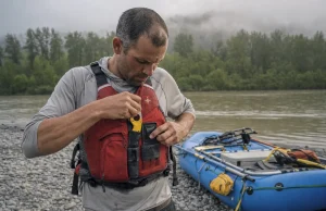 River Knife Buying Guide Why Sheaths Fail First Boater clipping a CRKT Bear Claw river knife onto his PFD lash tab at a gravel-bar put-in