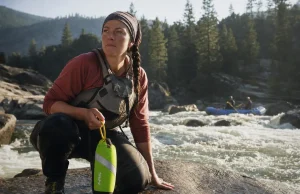 Best River Rescue Throw Bags and Why NFPA Is Overkill Rafter holding a high-vis green river rescue throw bag on a granite bank above a Class III rapid