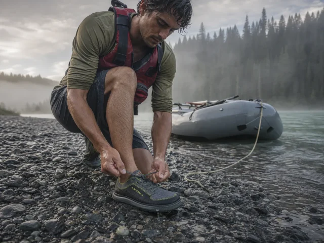 0-water-shoes-for-rafting-put-in Rafter lacing an Astral Brewer water shoe at a misty river put-in before launch