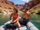 The Pro Rafter’s Guide to Inflatable Floor Types A fit couple in their late 20s on an inflatable raft on a sunny river, preparing their gear on the raft's floor.