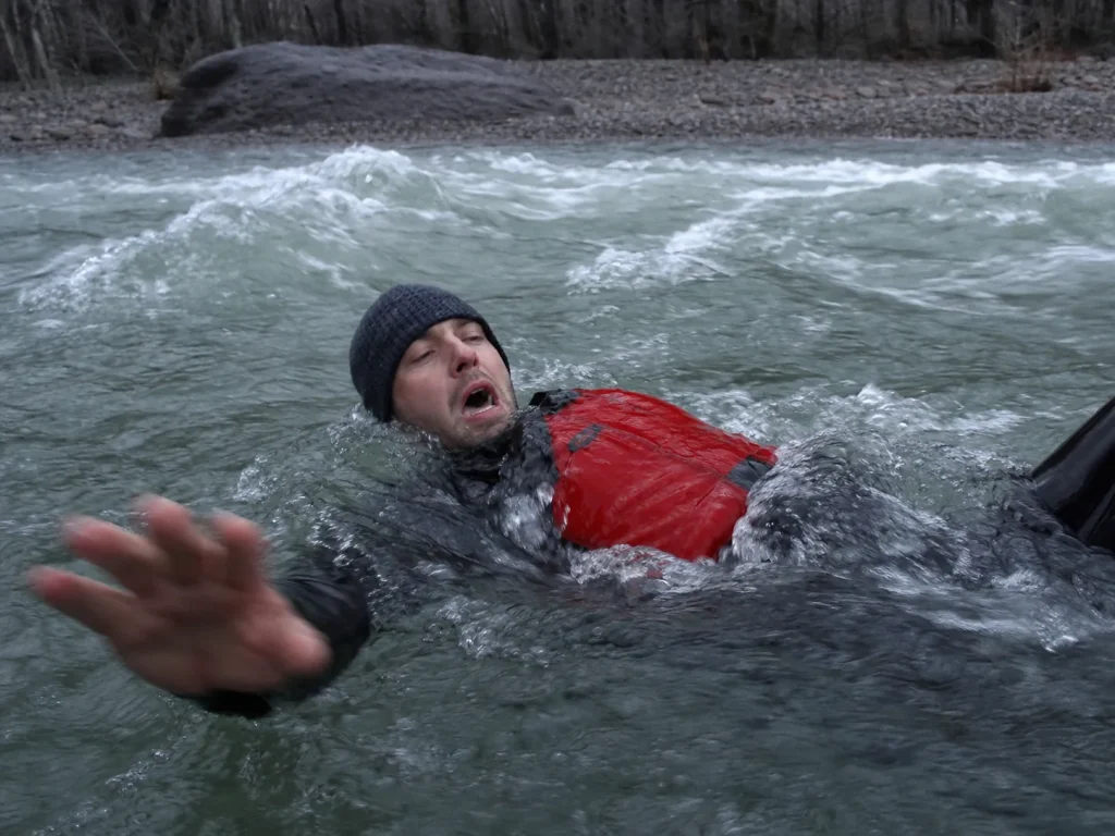 Rafter in the water in whitewater swim position in cold gray river after going overboard
