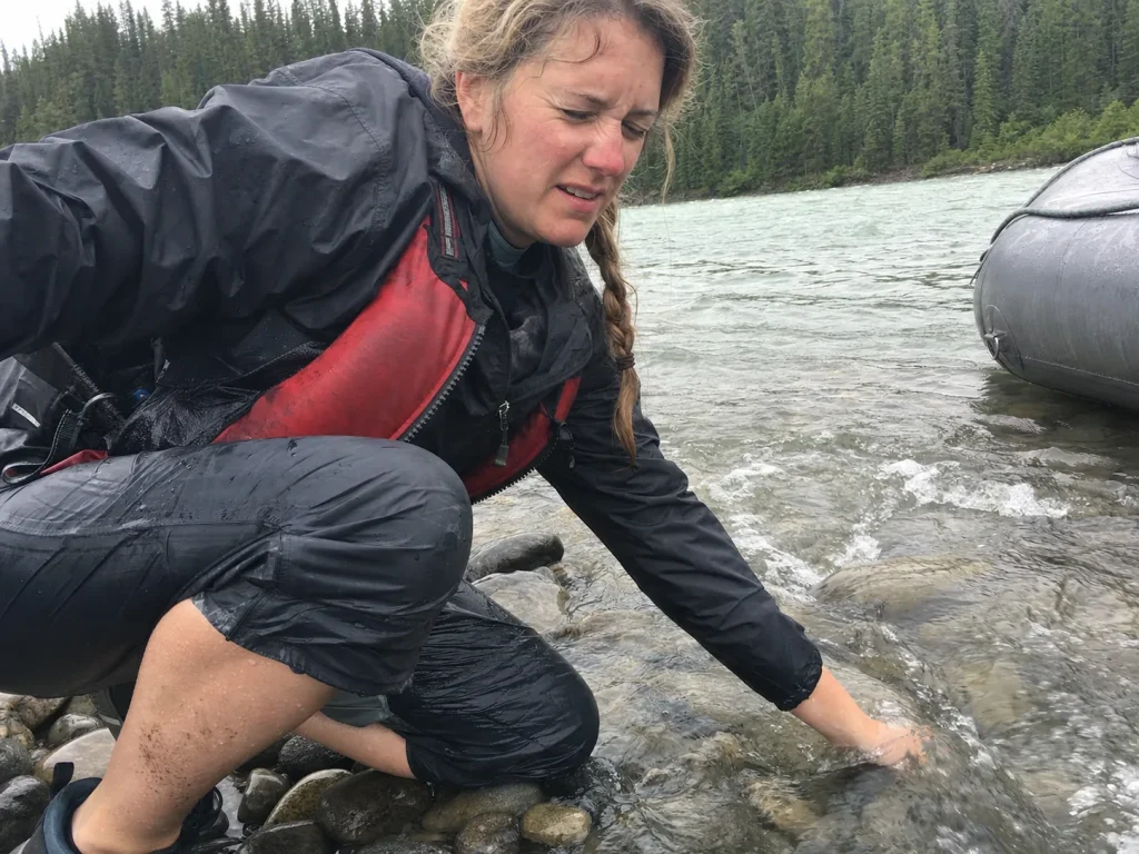 Rafter crouched at the river edge testing cold water temperature with a bare hand before a trip