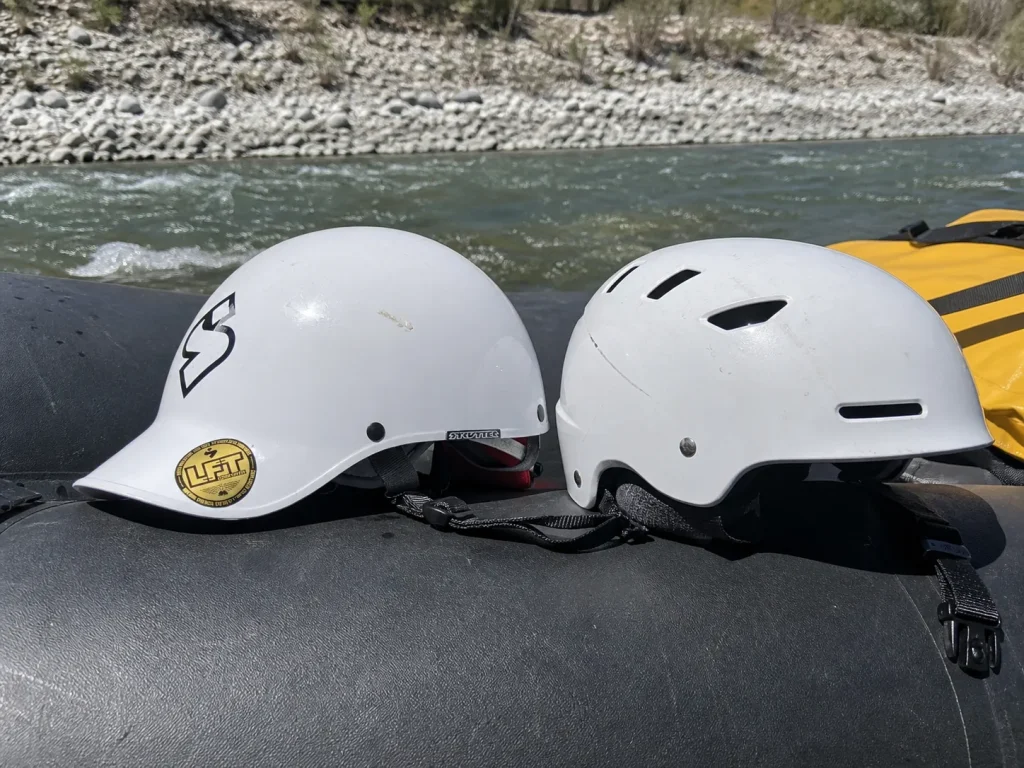 Half-cut Sweet Protection Strutter helmet set on a raft tube next to a full-cut helmet