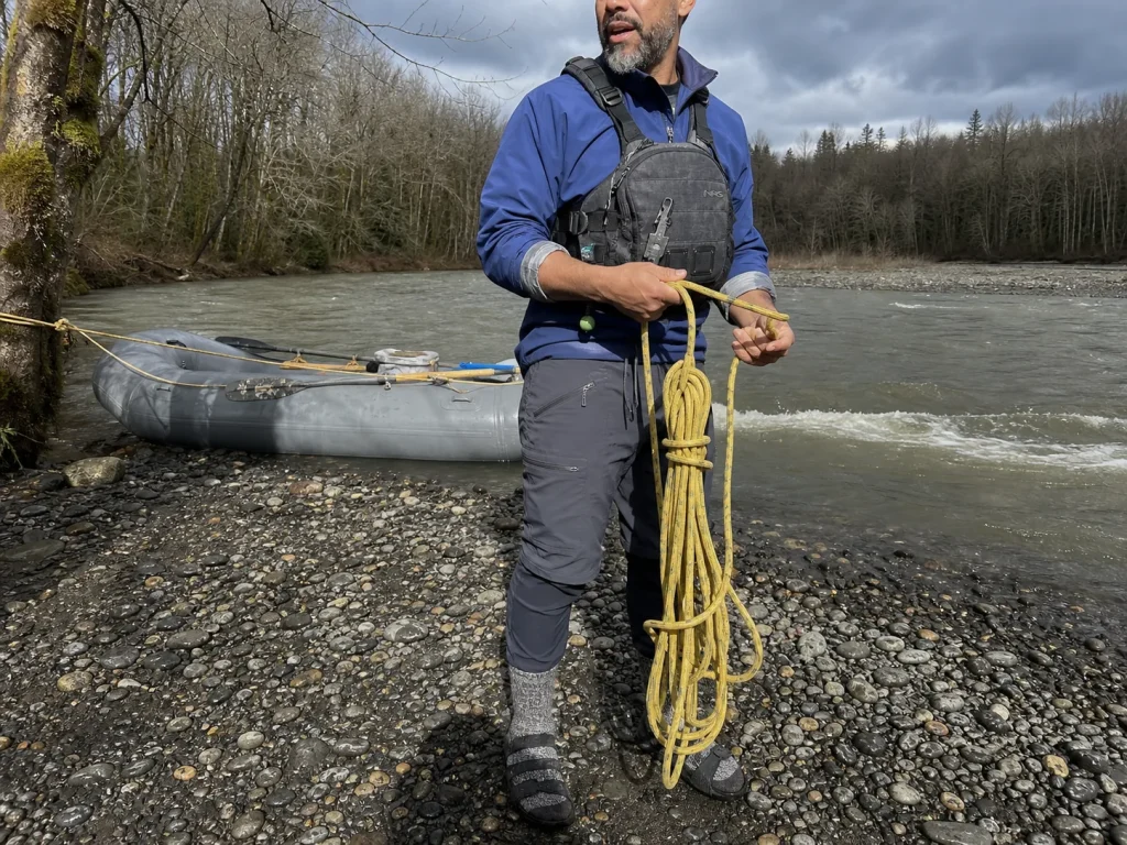 Boater coiling rescue rope on a gravel bar with an NRS Pilot Knife riding on his PFD