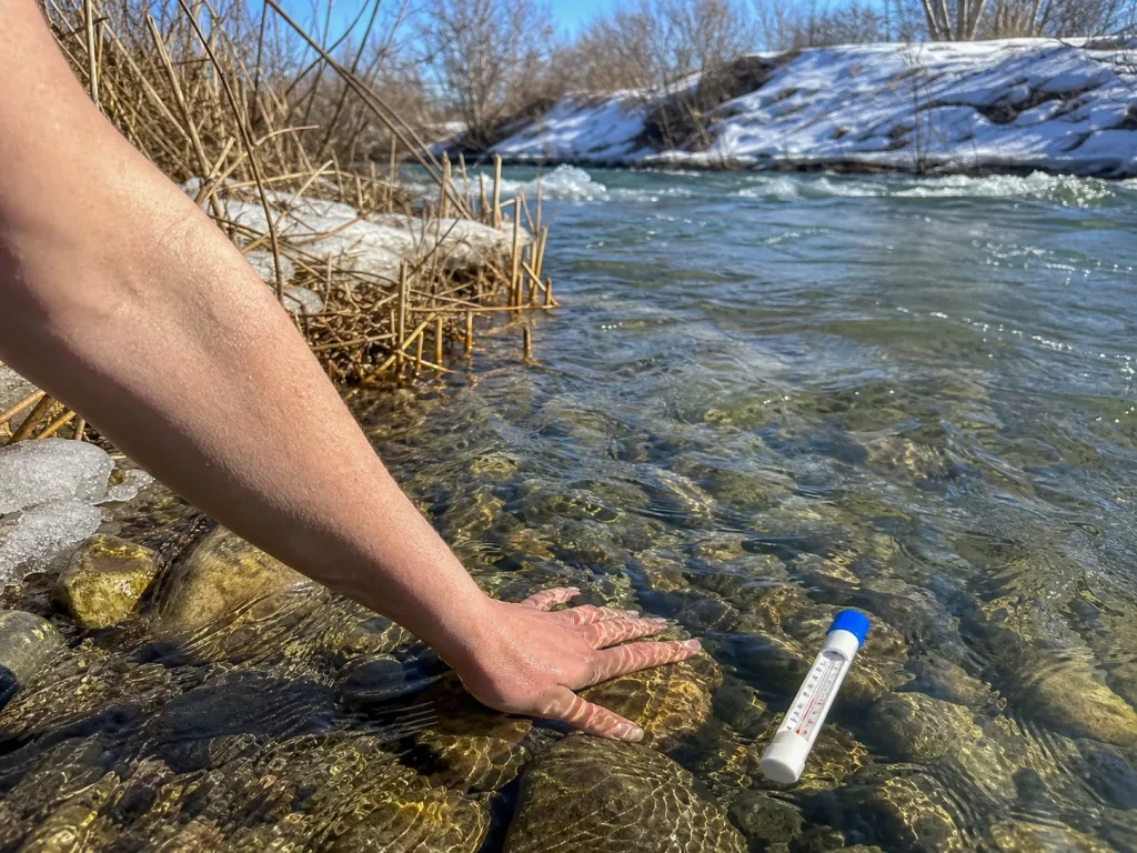 Hand dipping into cold snowmelt river at the bank to check water temperature before rafting
