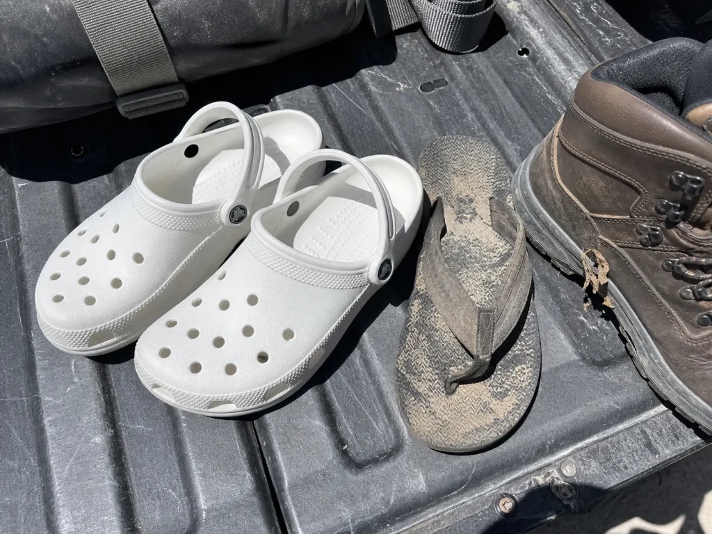 Loose Crocs and flip-flops set aside on a truck tailgate as the wrong rafting footwear