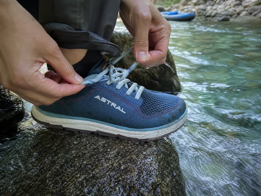 A rafter double-knotting a closed-toe river shoe lace tight before stepping into current