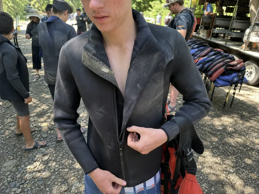 First-time rafter checking the zipper on a worn rental wetsuit handed out at the put-in