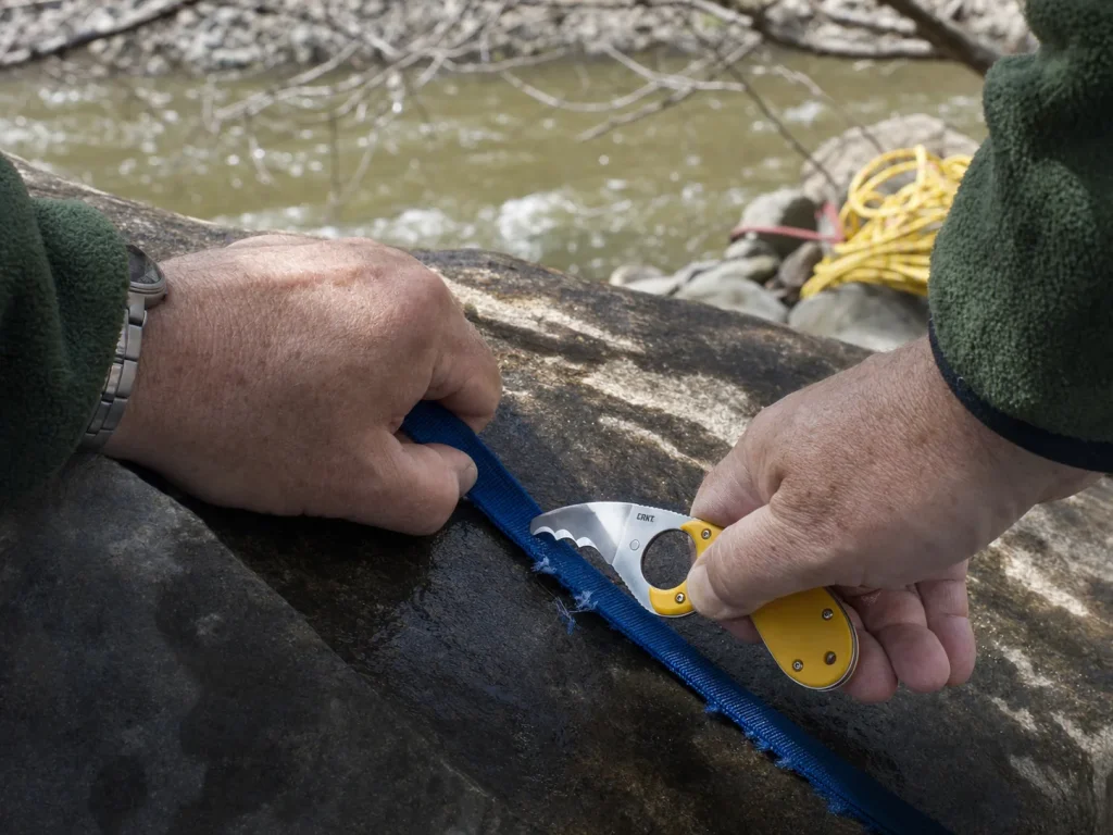 Serrated CRKT Bear Claw blade sawing through a wet loop of tubular webbing on a rock