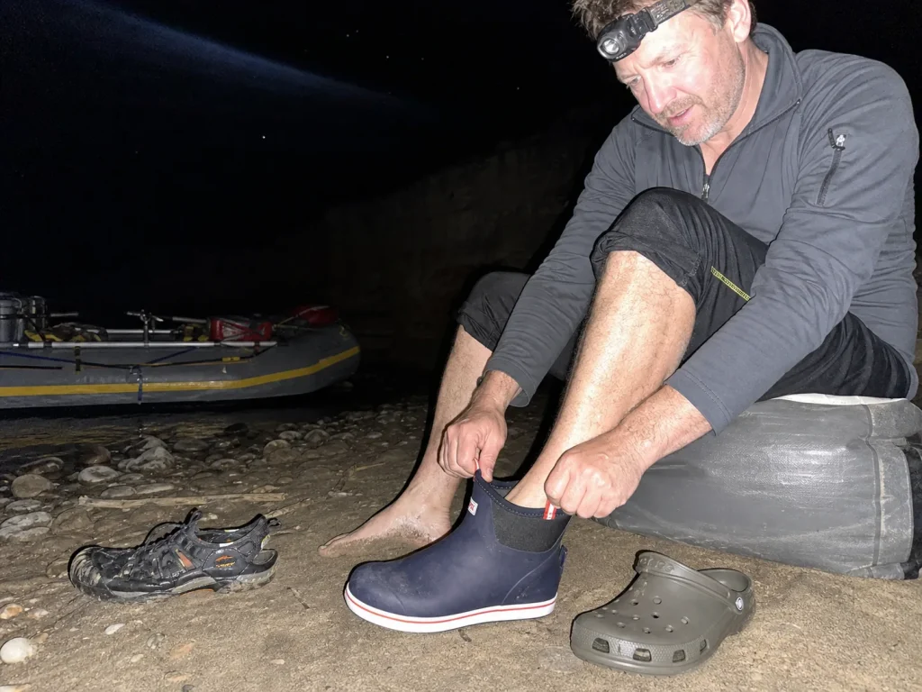XTRATUF camp boots and a Croc pulled on at a river camp at dusk after the water