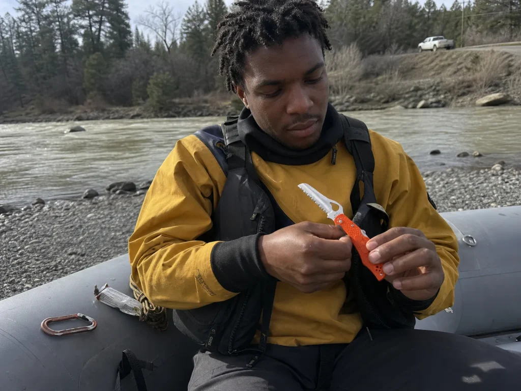 Boater opening a Byrd Cara Cara 2 Rescue folding knife two-handed beside a rigged raft