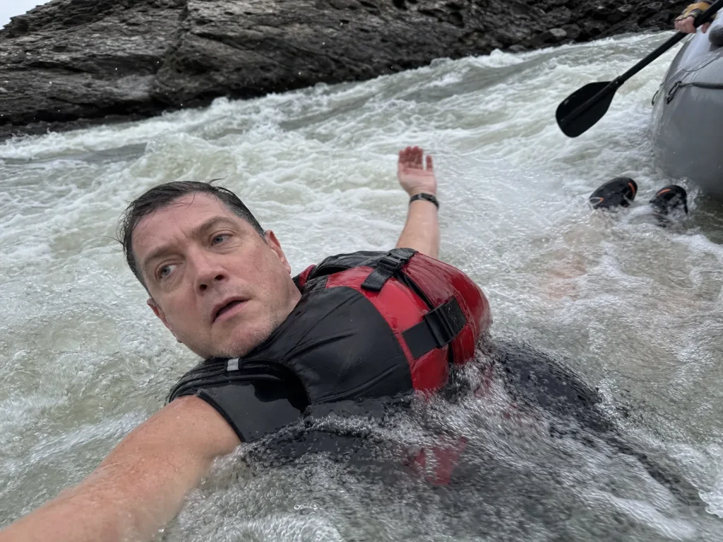 Whitewater swimmer floating feet-up and nose-downstream in a wetsuit and PFD after falling out