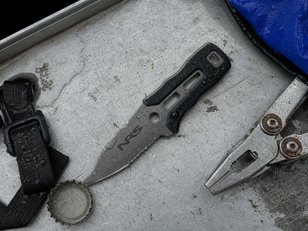 NRS Titanium Co-Pilot knife lying beaded with water on a wet aluminum dry box lid