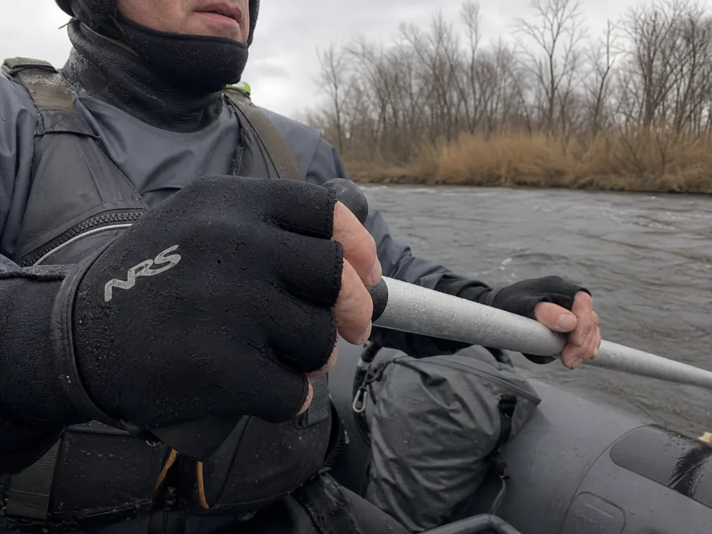 Rafter in neoprene boater's gloves and beanie gripping an oar on a cold gray river