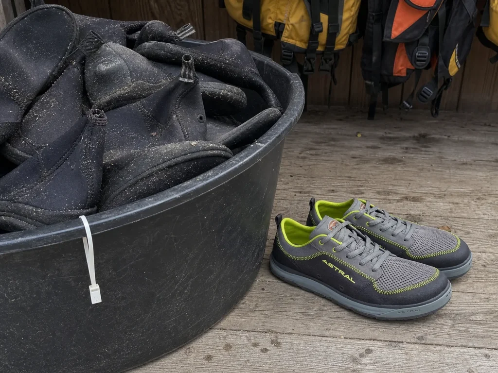 A worn pile of outfitter rental neoprene booties beside a rafter's own river shoes