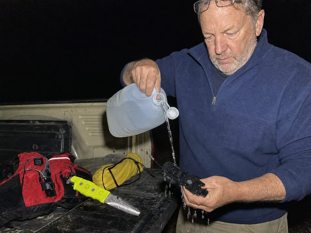 Boater rinsing a Gear Aid AKUA knife and its sheath at a truck tailgate at dusk