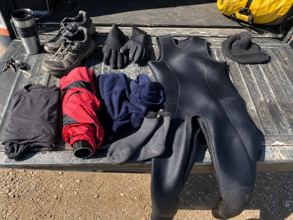 A budget cold-water rafting layering kit laid out on a tailgate before a trip