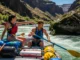 Advanced Oar Techniques: A River Runner’s Framework A fit couple in their late 20s rafting a sunny canyon, with the man using advanced oar techniques to maneuver the raft around a rock.