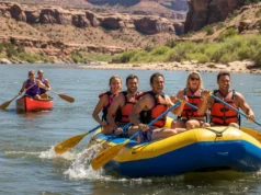 Canoeing vs Rafting: A Rafter’s Definitive Comparison A wide river scene with a large raft full of people in the foreground and a two-person canoe in the background, comparing the two watercrafts.