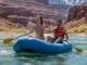 Cold Water Rafting: The Temperature-Specific Layering System An attractive young couple in their late 20s enjoying a sunny day of rafting on a cold, clear river with mountains in the background.