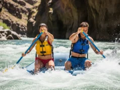 The Paddling Strength Audit: A Guide for Dedicated Rafters A fit couple in their late twenties wearing PFDs and swimwear paddle hard through whitewater rapids in a bright, sunny canyon.