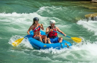 Mastering the Downstream V: A Foundational Rafting Skill A fit young couple in a raft navigate a whitewater rapid, following the clear path of a downstream V.