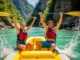 Europe’s Rivers: A Rafter’s Guide from Class II to V A fit young couple in a whitewater raft celebrate with paddles in the air on a beautiful emerald river in Europe.