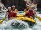 The First-Timer’s Rafting Trip Protocol: A Field Guide A full-body, wide-angle view of four young adults in a yellow raft, paddling together with excitement through whitewater rapids on a sunny day.