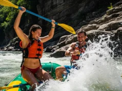 Gauley River Rafting Guide: Upper vs. Lower & Outfitters A man and woman in a full-body view, wearing swimwear, celebrate excitedly while whitewater rafting through a rocky river canyon.