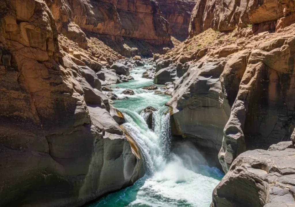 A steep riverbed in a canyon showing visible rock layers and ledges that create a powerful rapid.