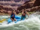 Grand Canyon Itinerary Mapped: Rafting by Skill Level Full-body shot of a young couple rafting through a major rapid in the Grand Canyon, with towering red rock walls in the background.