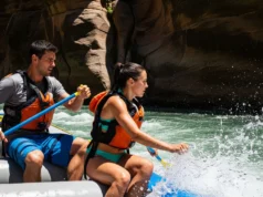 Guiding a Raft: From Basic Strokes to River Reading A full-body shot of a fit man and woman in their late 20s guiding a raft through whitewater rapids on a sunny day.