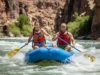 Rafting History: From Rapids to River Conservation A full-body shot of a young man and woman in their late 20s laughing as they paddle a raft through whitewater rapids in a sunny canyon.