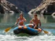 Laminar vs Turbulent Flow: A Rafter’s Guide to River Reading A fit couple in their late 20s rafting on a sunny river, moving from a calm, glassy section of water towards turbulent whitewater rapids ahead.