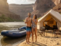 The Luxury Rafting Index: Ranking Trips & Outfitters A full-body shot of a fit couple in their late 20s toasting with drinks on a river beach, with a luxury raft and safari-style camp behind them.