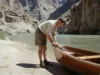 The Anatomy of a Martin Litton Dory: A Deep Dive A vintage-style photo of a man working on his wooden dory on a riverbank inside the Grand Canyon.