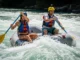 Mastering Rafting Safety: A Class I-V River Guide A fit couple in their late 20s, wearing PFDs and helmets over swimwear, confidently paddling a whitewater raft through a sunny rapid.