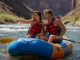 Mastering Rafting Terms: A Guide to River Communication A fit couple in their late 20s on a whitewater raft, with the woman pointing downriver to explain a river feature.